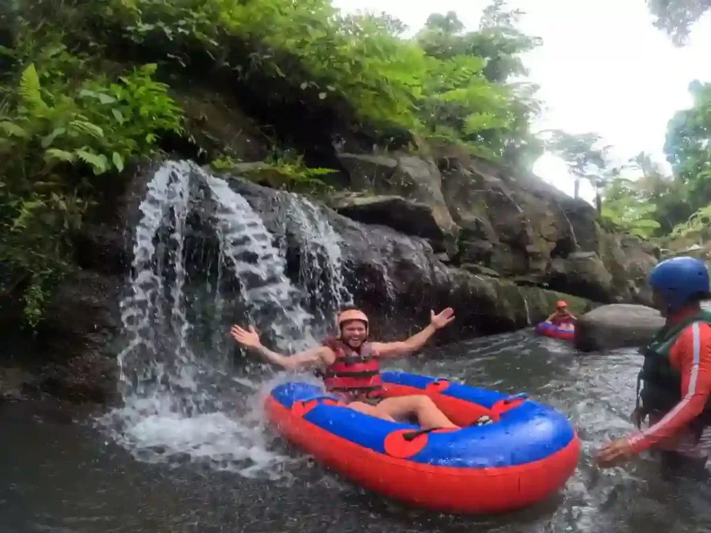 Tourist smiling on an inner tube beside a waterfall on the Tubing Adventure Ubud route